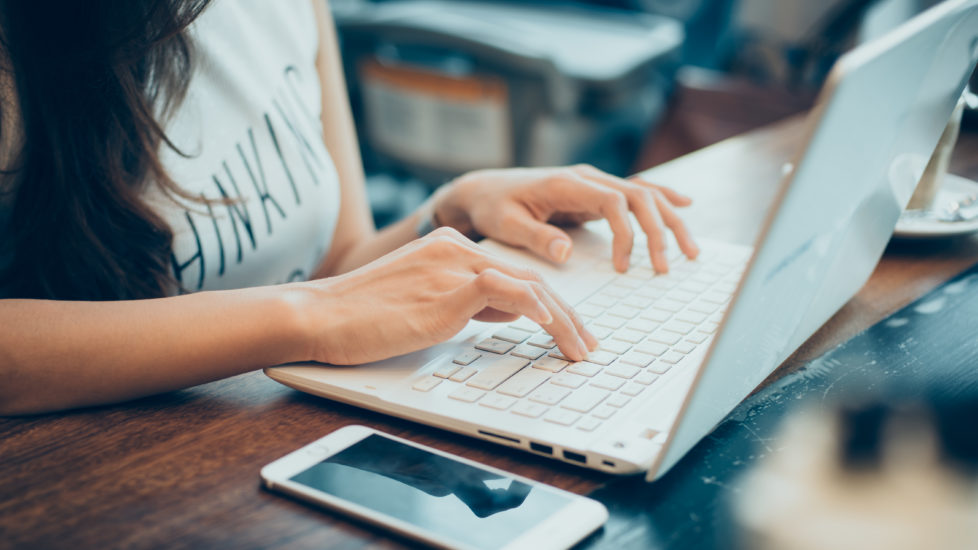 beautiful young hipster woman's hands busy working on her laptop sitting at wooden table in a coffee shop