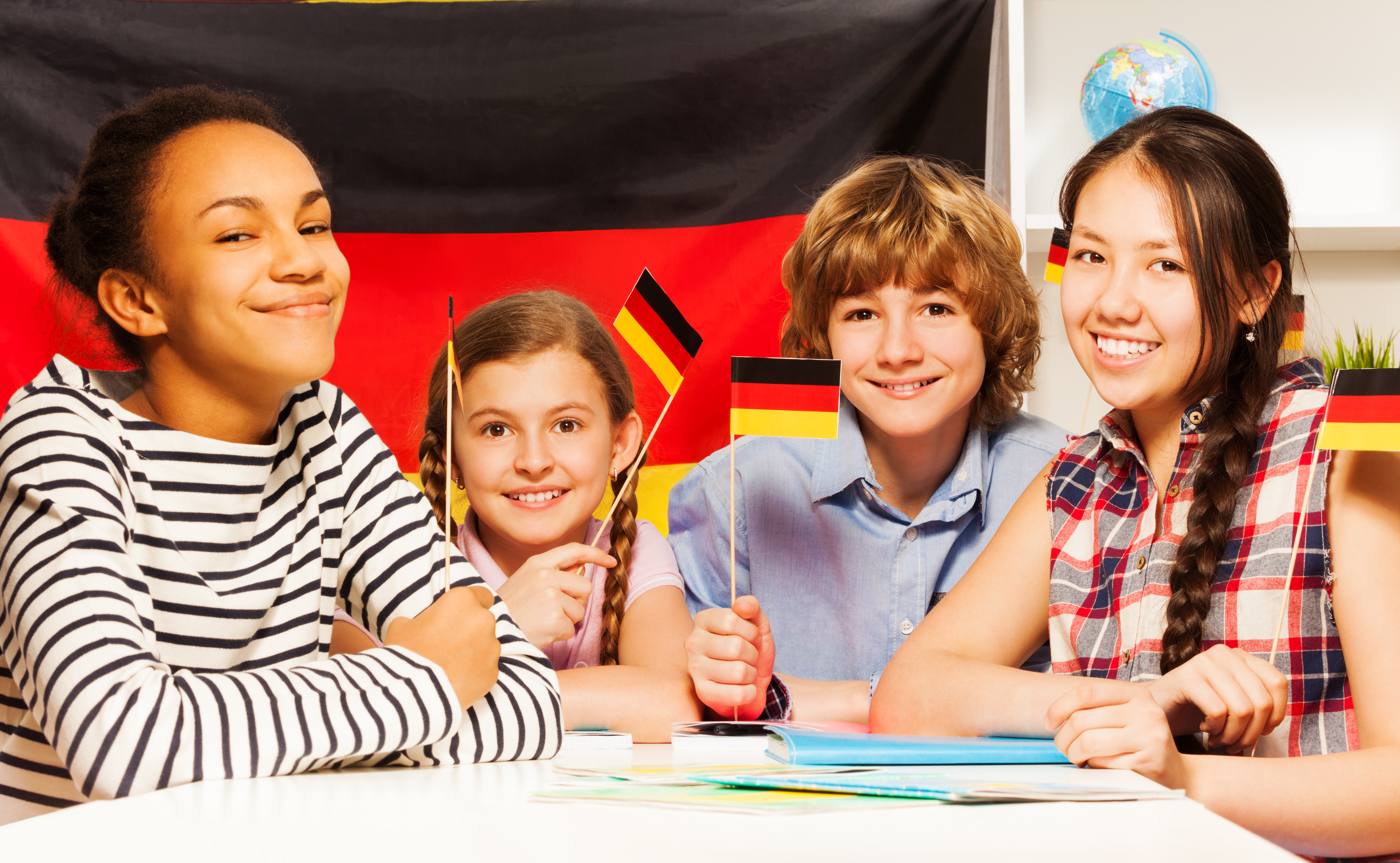 Four happy multiethnic teenage students waving German flags at the language courses